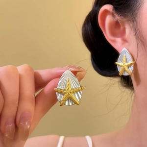 Detailaufnahme eines Ohrsteckers mit goldenem Seestern und silberner Muschel auf Modell.