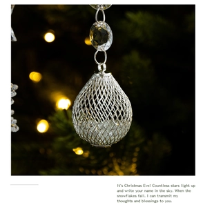 Close-up of a silver waterdrop Christmas ornament with crystals on a lit tree