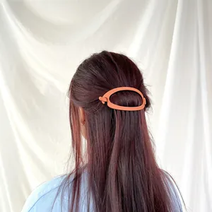 Detail of matte orange hair claw clip on long reddish brown hair with oval hollow design