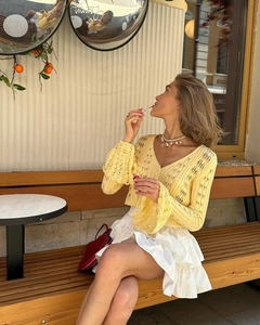 Detail of the knit cardigan with V-neckline and ruffled hollowed cuffs in yellow