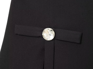 Detail of a large faceted crystal button on black woven fabric with ribbon trim