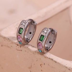 Gros plan de boucles d'oreilles argentées avec zircons colorés sur pierre texturée