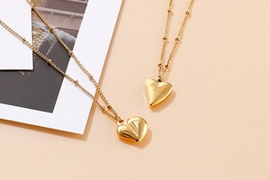 Makroaufnahme einer goldenen Herzhalskette mit Strukturdetails auf rosa Grund