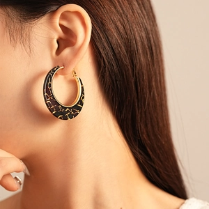 Close-up of retro black and gold resin geometric earrings worn by model on ear