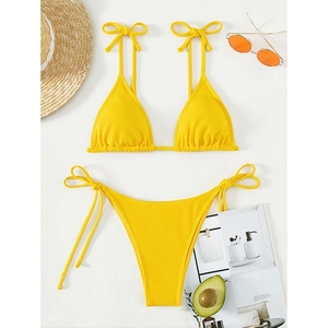 Yellow ribbed two-piece bikini set with bow details and beach accessories on white background