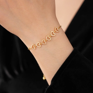 Gros plan d'un bracelet doré avec breloque cœur et zircons porté au poignet d'une femme