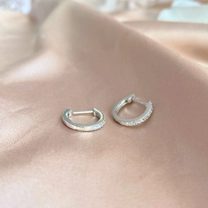 Macro shot of silver S925 earrings with sparkling zircons on elegant champagne silk fabric