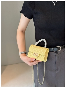 Detail of yellow mini bag with quilted pattern, pearl handle, and golden chain strap