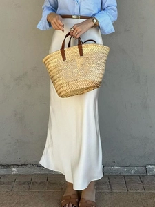 Elegant white maxi bodycon skirt in silk texture styled with a brown belt and straw tote