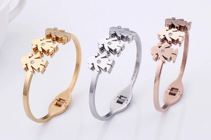 Close-up of three open metal bracelets in gold, silver, and rose gold with girl charms