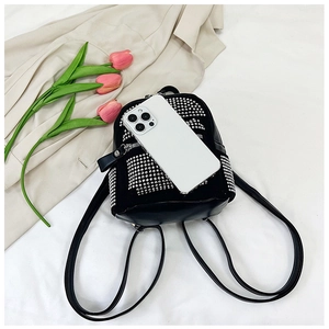 Detalle de una mini mochila negra con tachuelas plateadas junto a un móvil para el tamaño