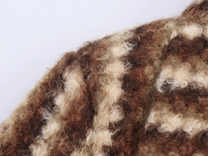 Gros plan détaillé sur la texture du tissu bouclé marron et beige de ce manteau