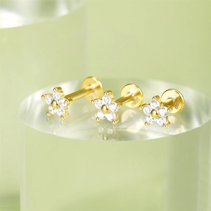 Detailed view of three gold flower stud earrings with white zircons on clear base