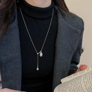Y-shaped silver pea pendant pearl necklace layered over a black turtleneck top