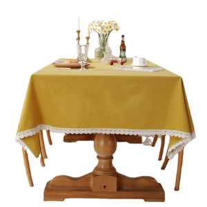 Modern mustard yellow cotton tablecloth with white lace edges on a wooden dining table