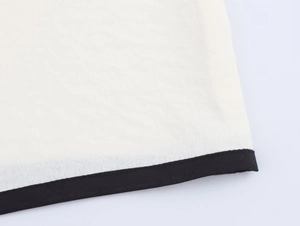 Close-up of cream textured crepe fabric with contrasting black stitched trim detail