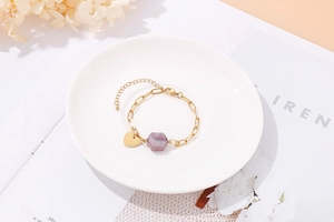 Detail of adjustable gold bracelet featuring a purple gemstone and heart charm on white tray