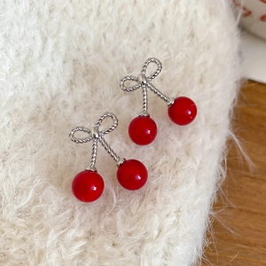Macro shot of sweet cherry earrings with red resin beads and a silver bow on white knit