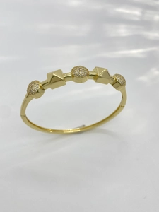 Detailed close-up of golden bangle with pyramid blocks and pave crystal spheres