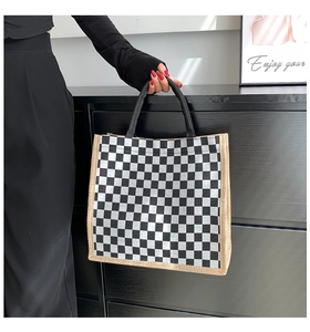 Close-up of black and white checkerboard tote bag with beige linen trim held by hand