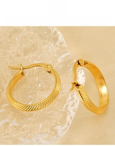 Macro shot of gold-plated titanium steel hoop earrings with diagonal striped texture