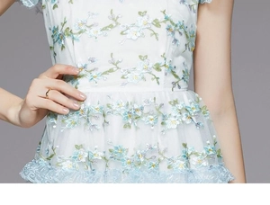 Détail de broderie florale bleu clair sur robe en dentelle avec volants étagés