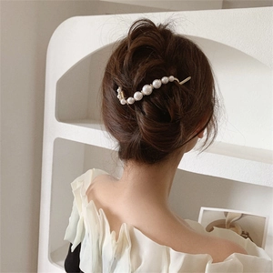 Detail of white pearls on golden S-shaped hair clip worn in a minimalist hairstyle
