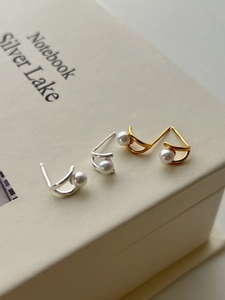 Detail of 925 silver pearl stud earrings in gold and silver set on a leather book