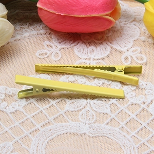 Close-up of yellow matte metal alligator hair clips on a white floral lace background
