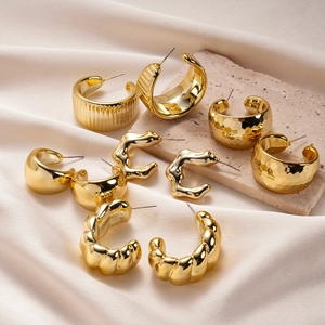 Set of ten geometric golden C-shaped stud earrings on silk and stone background