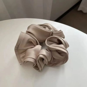 Detailed view of the champagne gold satin scrunchie with layered ruffles on a white table