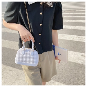 Outdoor street shot of white shell-shaped jelly bag with gold chain strap and top handle