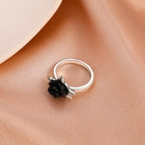 Top view of a silver black rose ring with leaf texture on elegant champagne silk fabric