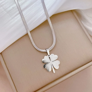 Macro detail of silver four-leaf clover pendant on snake chain inside jewelry box