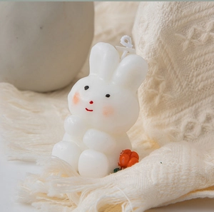Macro detail of white rabbit-shaped candle on beige tassel fabric with soft light