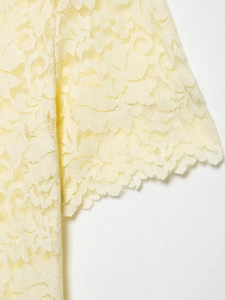 Close-up detail of pale yellow floral lace texture and scalloped edges on the sleeve