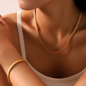 Detailed view of 18K gold plated woven chain necklace and bracelet worn by a model