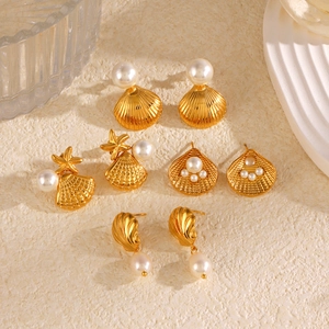 Ocean-themed gold earrings set with sea star and pearl charms on a ceramic tray