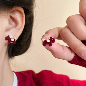 Detailed close-up of a burgundy flocked pony stud earring with gold accents on ear