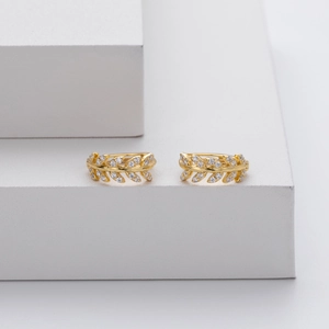 Detail of gold leaf earrings with white zircon accents on a white geometric block