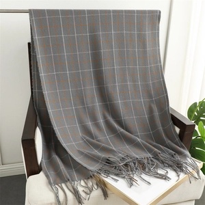 Close-up of grey plaid scarf with orange accents and tassels on a wooden chair