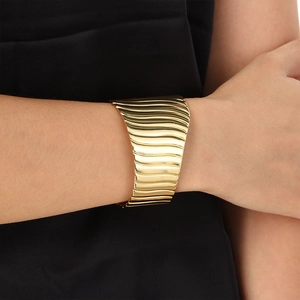 Macro detail of wide gold stainless steel cuff featuring elegant wavy textured stripes