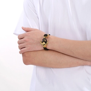 Detail of man wearing a black braided leather anchor bracelet with a gold metal clasp