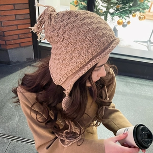 Close-up of knit winter earflap hat with decorative fringe and long braided ties