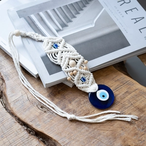 Detail of macrame evil eye wall hanging with white cotton rope and glass bead on wood