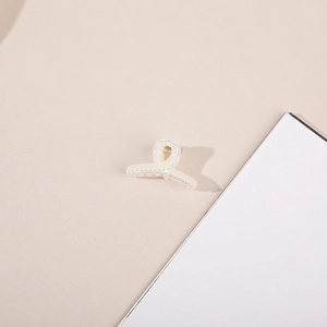 Detail of cross-wrapped hair claw clip with elegant embedded pearls on white finish