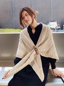 Detail of beige knitted shawl with brown leather buckle fastener on a model