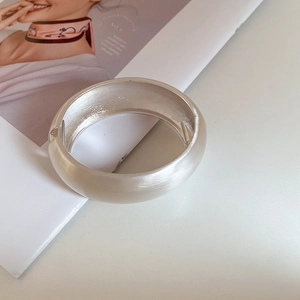 Minimalist wide brushed silver cuff bracelet with hinge closure on a fashion magazine