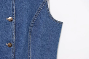Détail du gilet en jean bleu foncé avec boutons dorés et surpiqûres orange contrastées