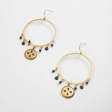 Close-up of golden boho hoop earrings with black beads and sunburst relief charm